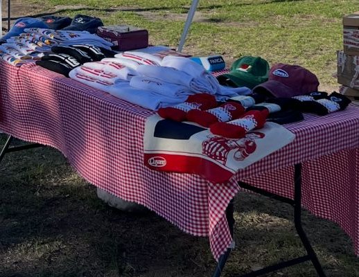 Mesa del stand con mantel cuadrillé, remeras dobladas, gorras y medias